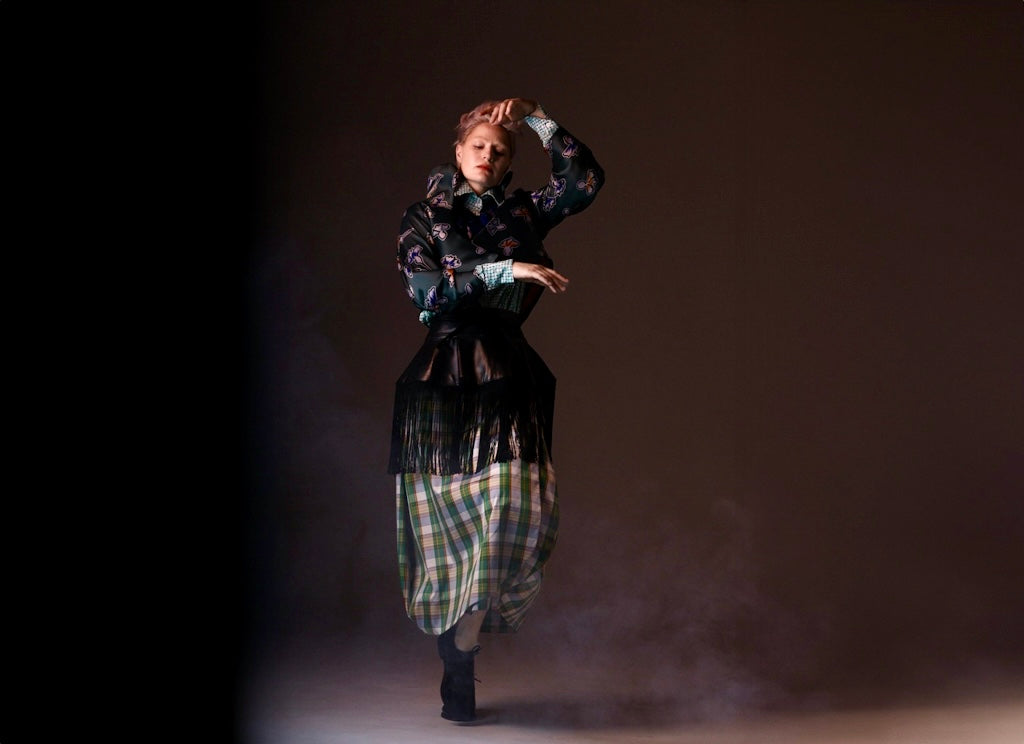 Person in a plaid outfit with a dark background dancing in Natalija Rushidi clothing 